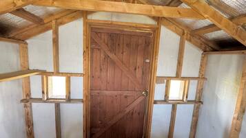A wooden door with a cross-brace design, a pitched roof with wooden beams, and a white wall with a window on the left.
