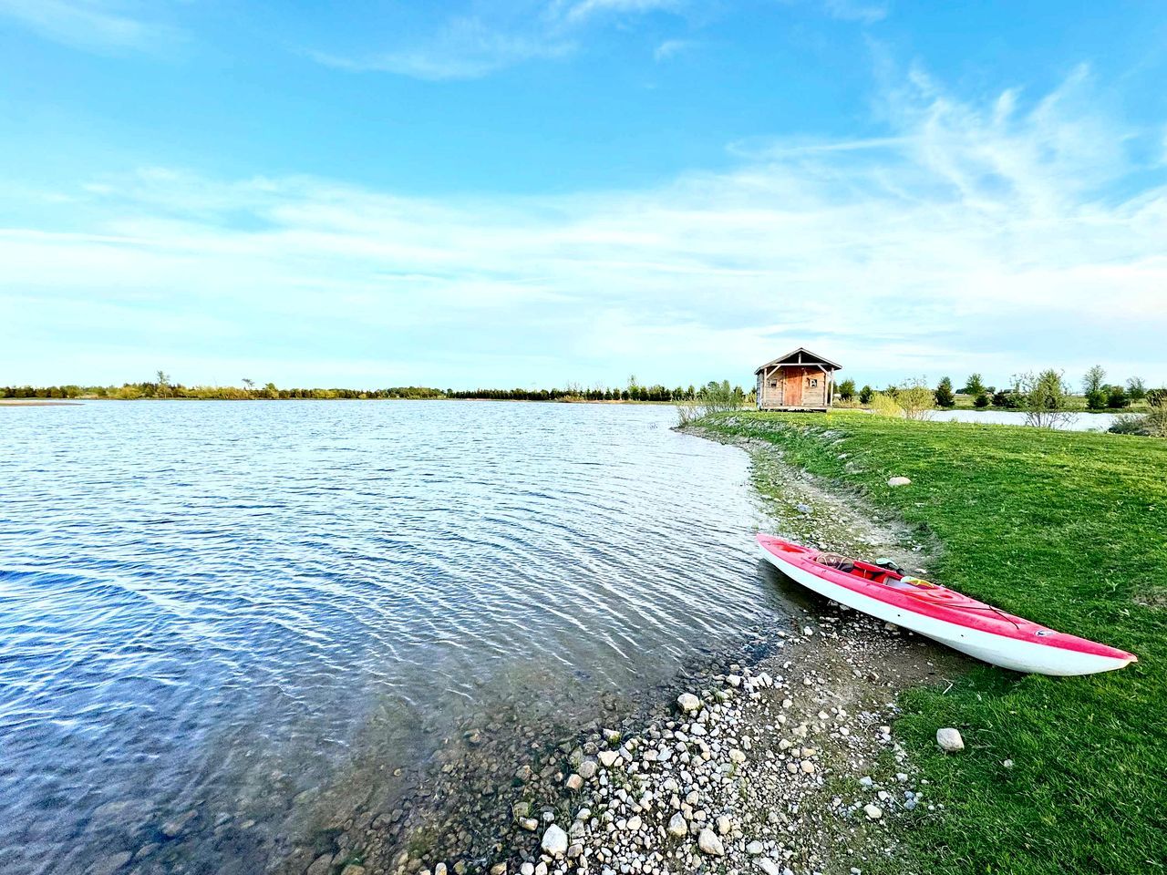 Un kayak sulla riva erbosa di un'acqua calma, con una casa sullo sfondo.