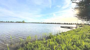 A calm lake with a dock, surrounded by grassy banks and trees.