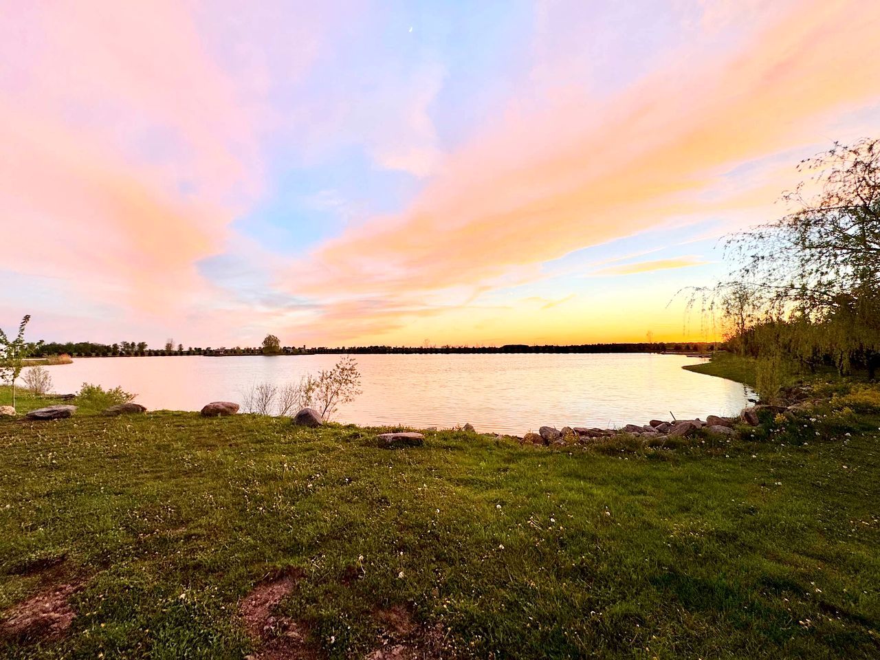 A lakeside view with a grassy foreground and a calm body of water.