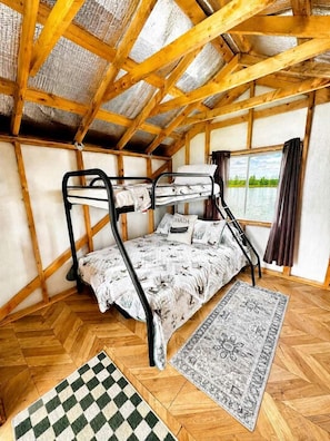A bunk bed room with a view of a body of water, wooden beams, and a patterned rug.
