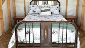 Una habitación con estructura de madera, una cama, una ventana con cortinas y suelo con estampado de espiga.
