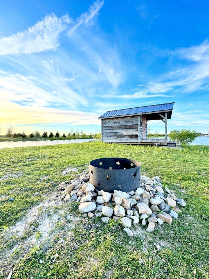 Un rustico chalet in legno con un braciere in metallo circondato da rocce, sullo sfondo di un cielo sereno.