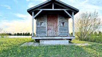 Una pequeña cabaña de madera con porche, ubicada en un campo cubierto de hierba bajo un cielo despejado.