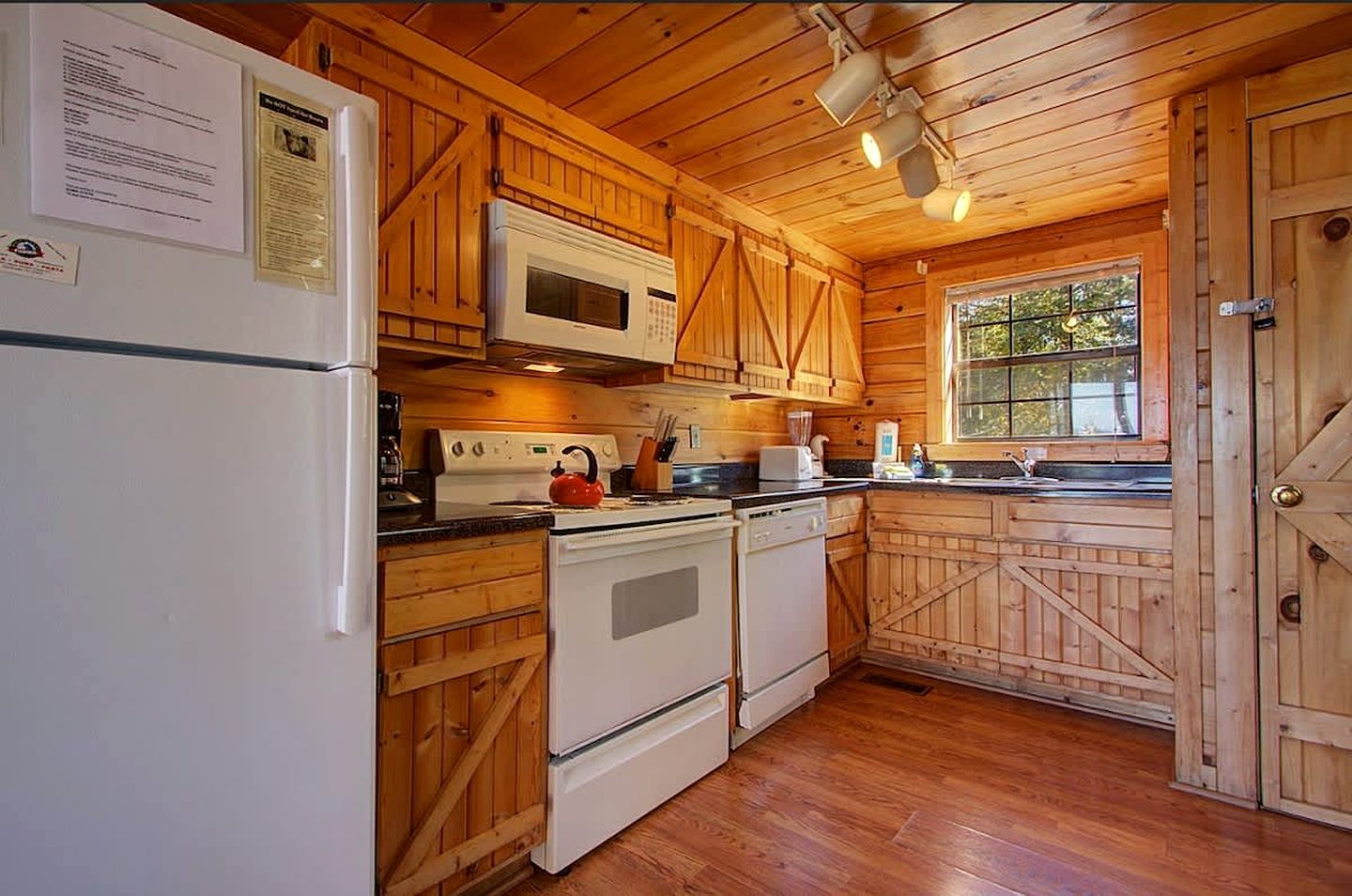 A kitchen with wooden cabinets, a refrigerator, a microwave, an oven, and a kettle.