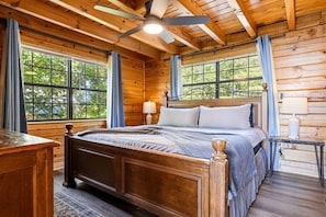 A wooden cabin bedroom with a bed, two bedside lamps, a ceiling fan, and large windows. - Extraordinary Smoky Mountain Cabin with Panoramic Views, Hot Tub & Arcade near Pigeon Forge and Gatlinburg, TN (Sevierville)