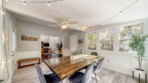 A dining area with a wooden table, four chairs, a ceiling fan, and large windows. - Spacious Cabin with Fire Pit, Arcade Games, and Resort Access, the Perfect Base for Outdoor Adventures in Hedgesville, West Virginia (Hedgesville)