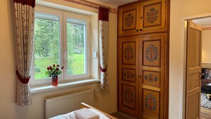 A bedroom with a bed, a window with curtains, a radiator, and a wardrobe with decorative panels.