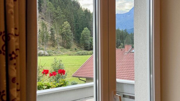 A balcony with a table and chairs, a view of a forested area, and a mountain in the distance.