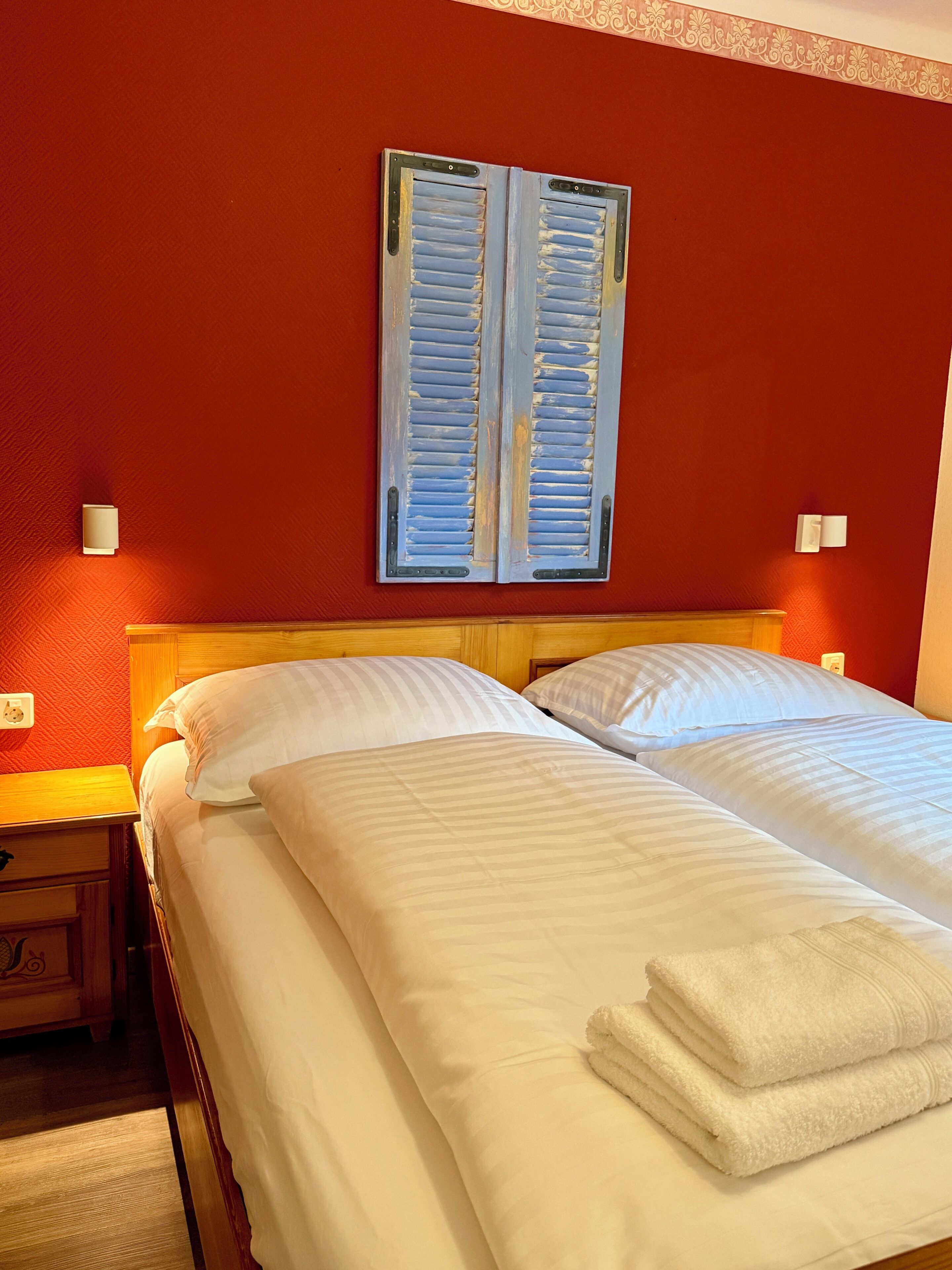 A hotel room with two beds, a wooden headboard, a red wall, and a decorative wall hanging.