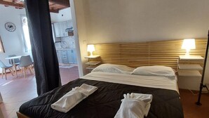 Ein Schlafzimmer mit einem Bett, zwei Nachttischlampen, einem Holzkopfstück und Blick auf eine Küche und einen Essbereich.