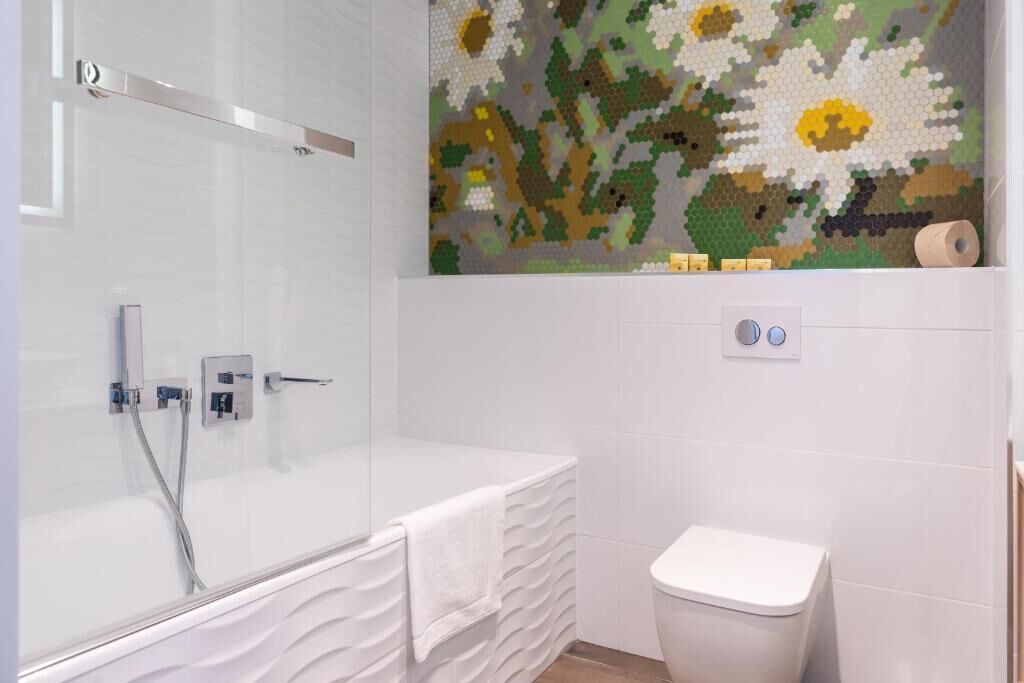 Ein modernes Badezimmer mit einer gläsernen Duschkabine, einer weißen Toilette und einer Mosaikwand.