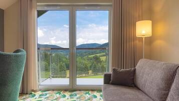 Habitació amb sofà, cadira, làmpada i finestra gran que mostra un paisatge verd.