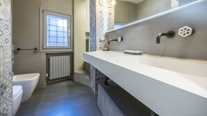 Ein modernes Badezimmer mit einem weißen Waschtisch, einem großen Spiegel, einer Toilette und einem Fenster.
