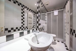 Une salle de bain avec un lavabo blanc, un miroir, des toilettes et un espace douche.