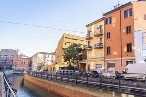 Un canal surmonté d’un pont piétonnier, des immeubles dotés de balcons et des voitures garées le long du quai.