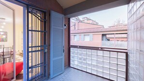 Een balkon met een metalen hekwerk, een schuifdeur en uitzicht op omliggende gebouwen.