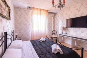A hotel room with a bed, a desk, a chair, a TV, and a chandelier. - Busacchi (Bologna)