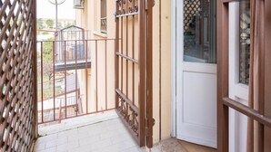 Ein schmaler Balkon mit Metallgeländer, einer weißen Tür und Blick auf eine Wohngegend.