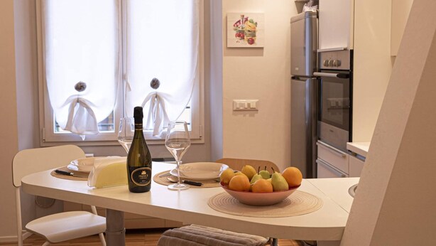Una mesa de comedor con una botella, una copa de vino, platos y un cuenco de fruta.