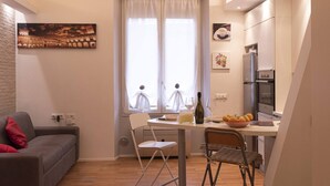 Un espacio habitable compacto con comedor, sofá, ventana con cortinas y zona de cocina con electrodomésticos.