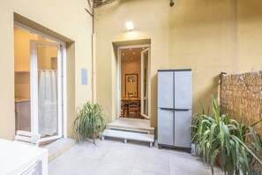 Un petit espace patio clos, doté d’une porte-fenêtre coulissante, d’un réfrigérateur, d’une table à manger avec des chaises et d’une plante en pot.