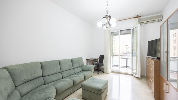 Ein Wohnzimmer mit einem Ecksofa, einem kleinen Tisch, einem Sessel und einem Fernseher auf einer Holzkommode.