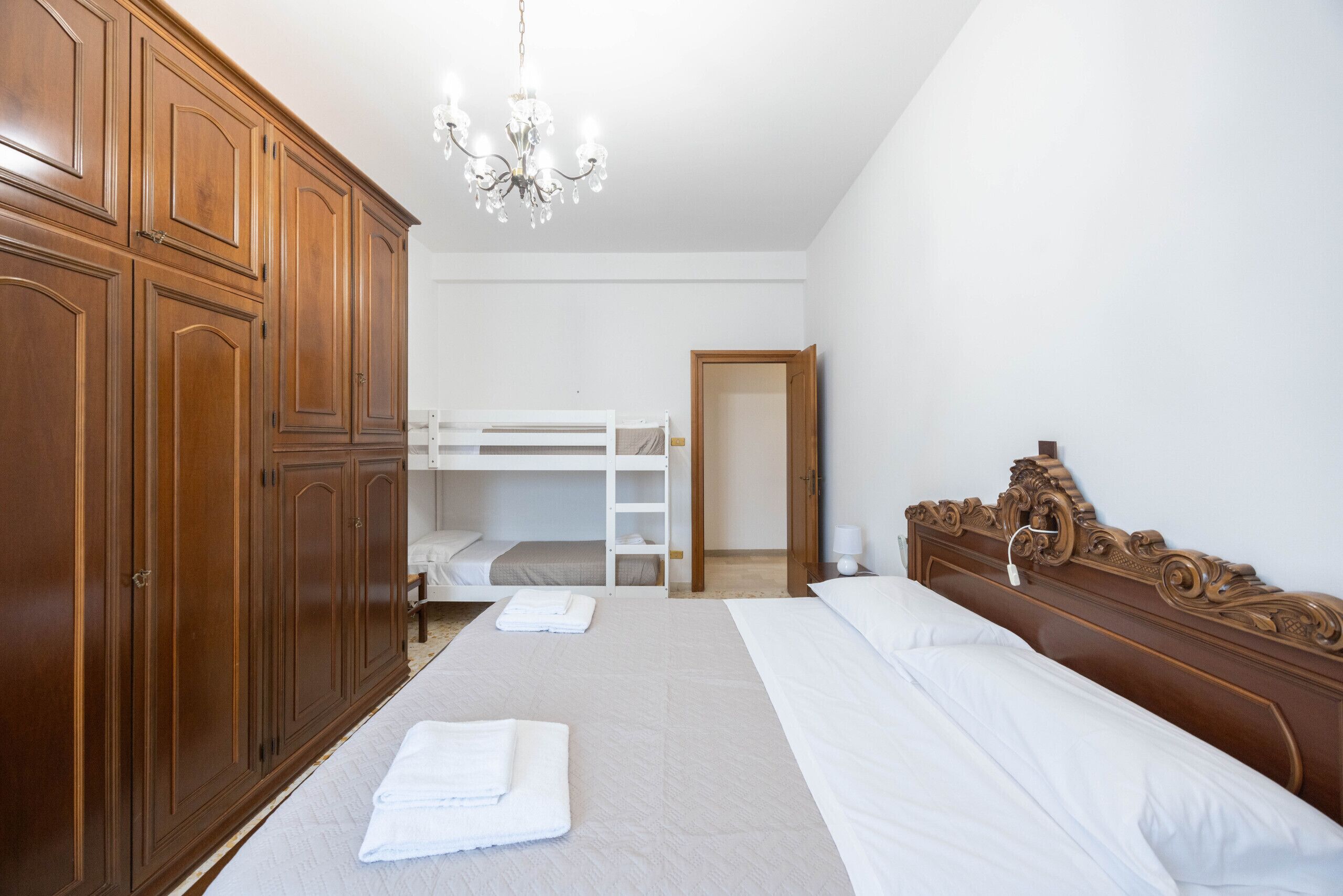 A bedroom with a bunk bed, wooden wardrobe, and a chandelier.
