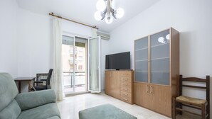 Ein Wohnzimmer mit einer Couch, einem Fernseher, einer Holzkassette und einem Balkon mit Blick auf Gebäude.