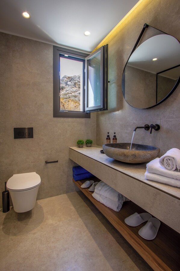 Un baño moderno con un lavabo de piedra, inodoro, espejo y ventana con vistas a un paisaje rocoso.