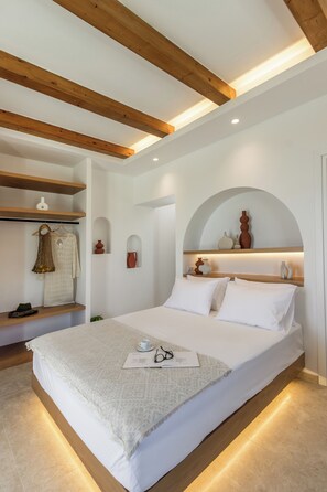 Um quarto moderno com uma cama grande, vigas de madeira, paredes brancas e uma estante embutida com objetos decorativos.