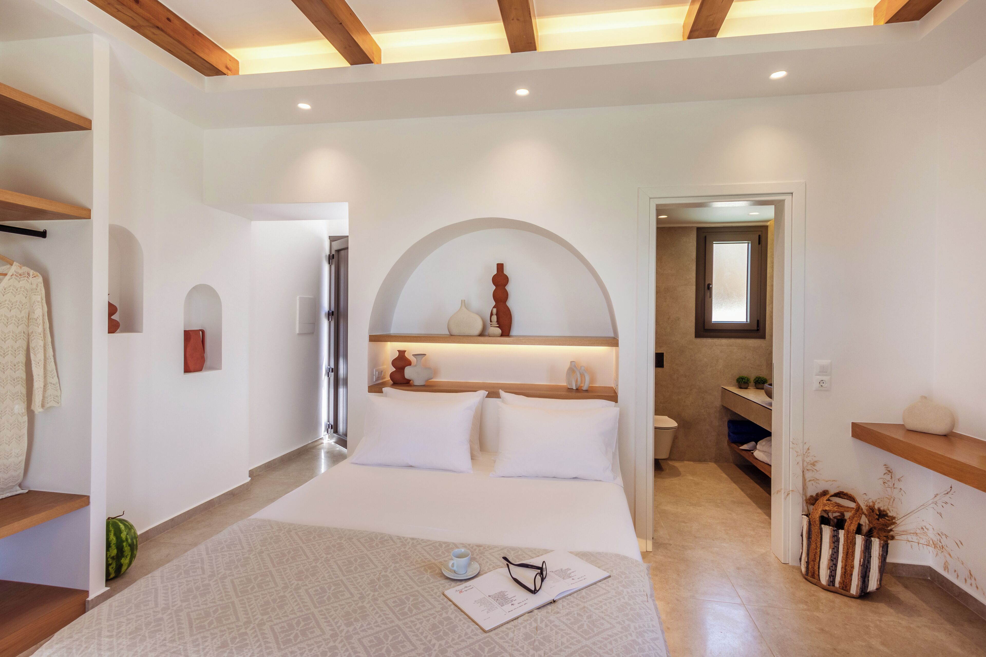 A modern hotel room with a large bed, a small seating area, a bathroom, and a wooden ceiling.