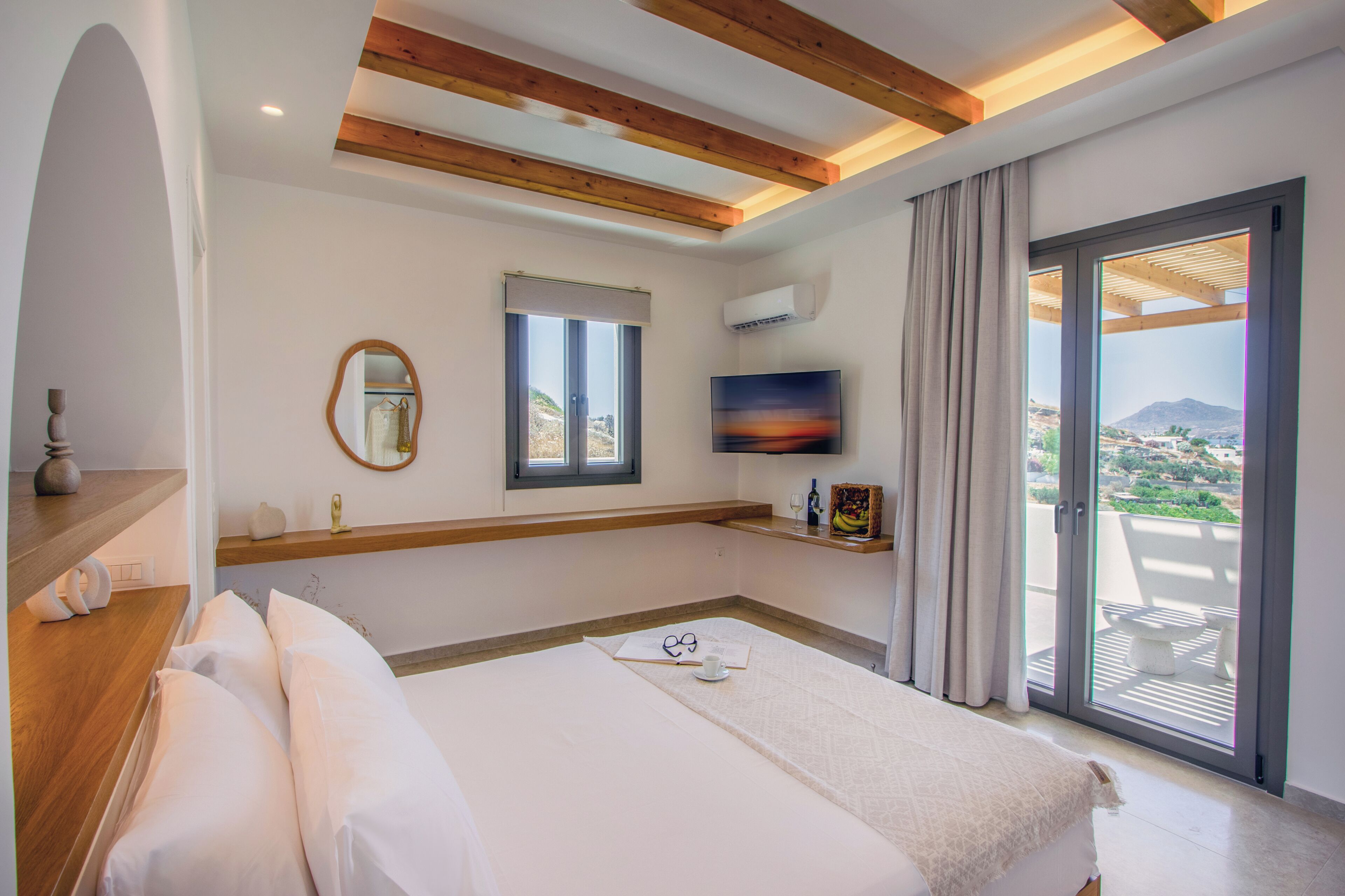 A bedroom with a bed, a TV, a window, and a balcony with a view.