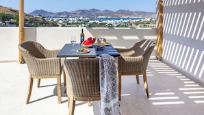 Une terrasse extérieure dotée d’une pergola en bois, de chaises en osier, d’une table avec une bouteille, des verres et une pastèque.