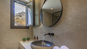 Une salle de bain avec un lavabo en pierre, un miroir, une fenêtre et un porte-serviettes.