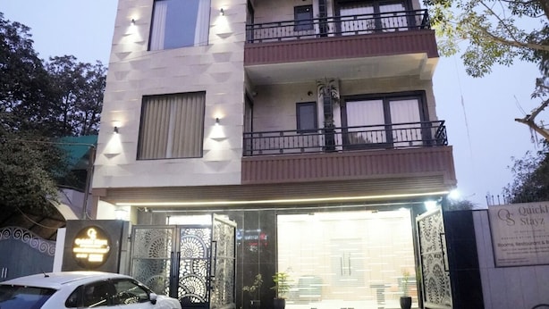 Ein mehrstöckiges Hotel mit moderner Fassade, einem begrenzten Eingangsbereich und einem weißen Auto vor der Einfahrt.