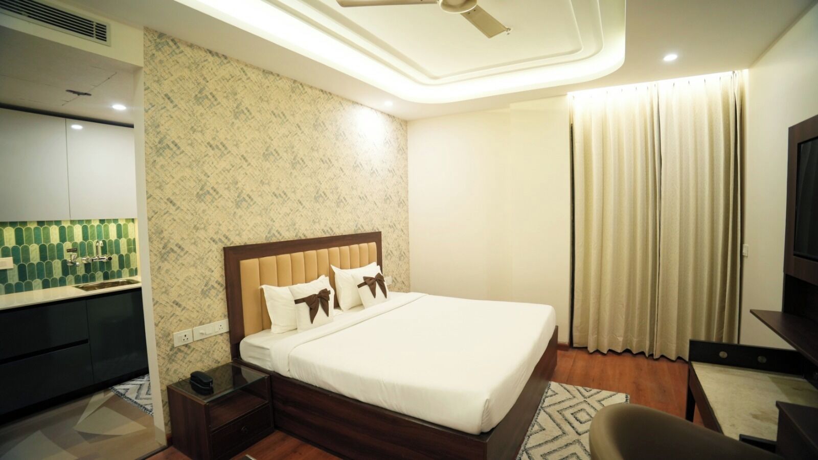 A hotel room with a bed, a TV, a desk, a chair, a nightstand, and a ceiling fan.