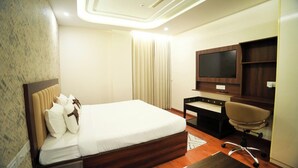 Ein Hotelzimmer mit Bett, Schreibtisch, Stuhl, Fernseher und einem kleinen Teppich.