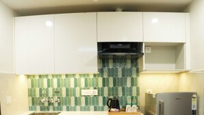 Eine kompakte Küche mit weißen Schränken, einem Edelstahlkühlschrank, einer gefliesten Spritzschutzwand und einer Kaffeemaschine auf der Arbeitsplatte.