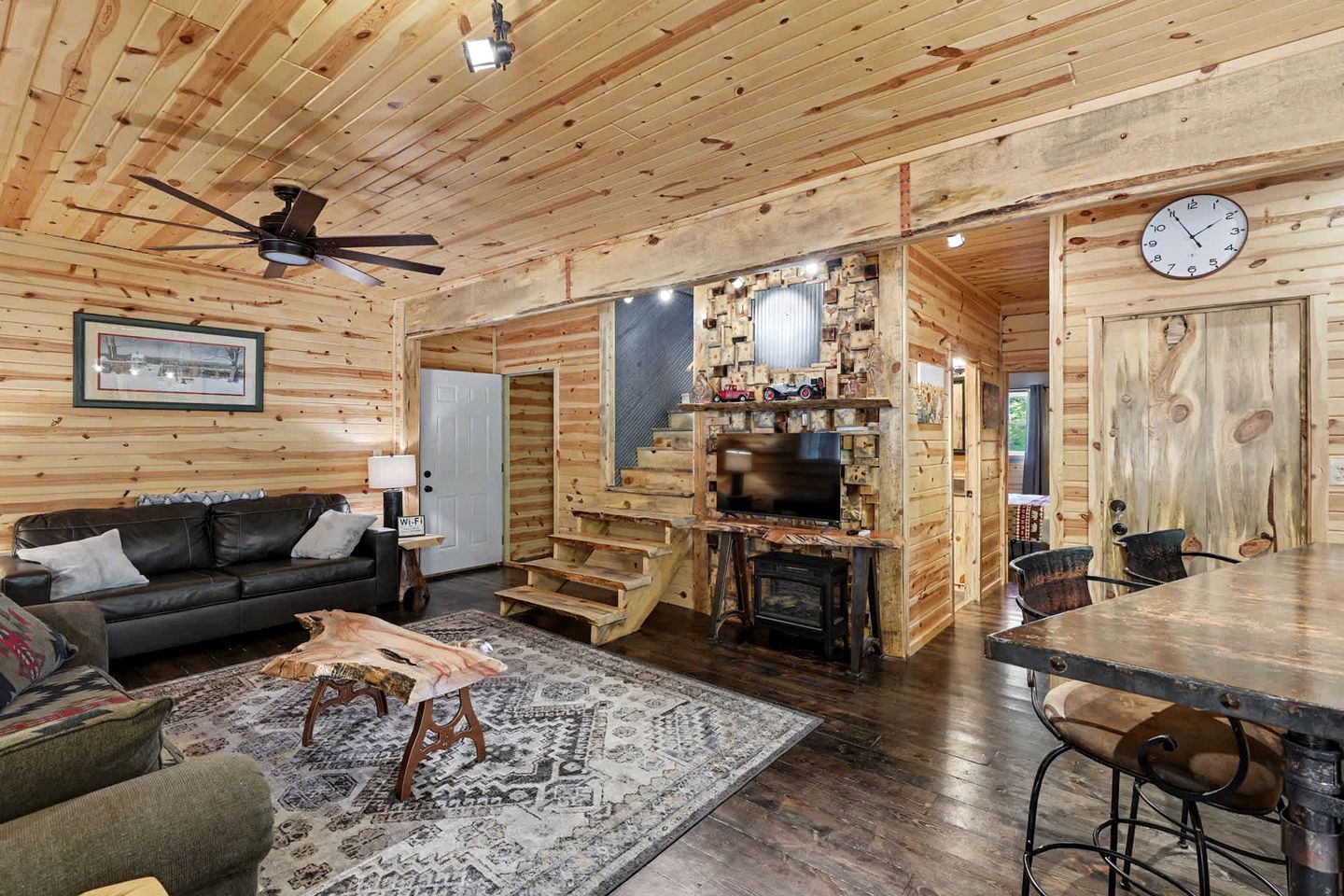 A log cabin interior with a living room, a fireplace, a staircase, and a dining area.