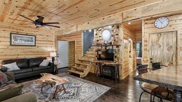 A log cabin interior with a living room, a fireplace, a staircase, and a dining area.