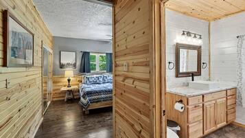 Una cabaña de madera con un dormitorio que tiene una cama, una mesita de noche y una ventana con cortinas.