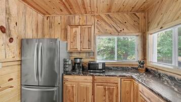 A kitchen with wooden cabinets, a stainless steel refrigerator, a coffee maker, a microwave, and a window with blinds.