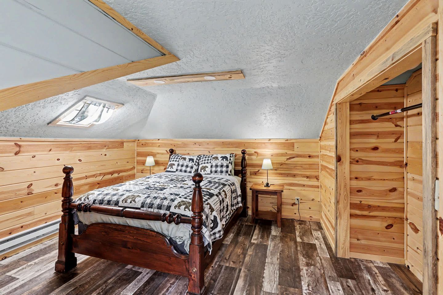 Een slaapkamer met houten lambrisering en een schuine hemel, een bed met een geruit sprei, twee nachtkastjes met lampen, en een dakraam.