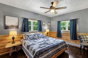 Een slaapkamer met een bed, twee nachtkastjes, een plafondventilator en ramen voorzien van gordijnen.