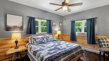 A bedroom with a bed, two bedside tables, a ceiling fan, and windows with curtains.
