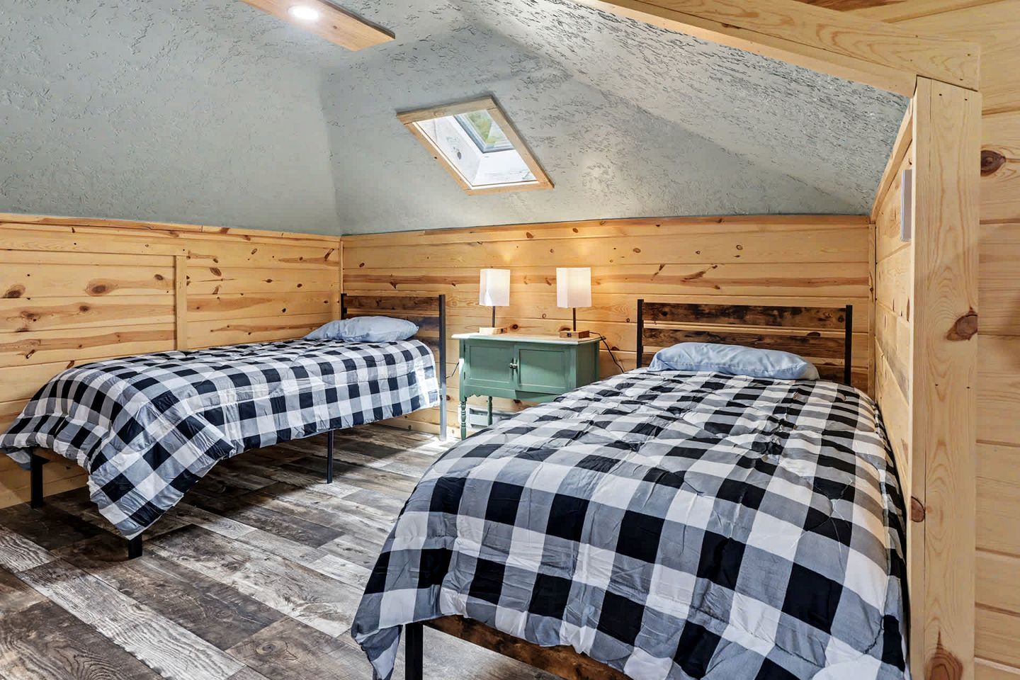 Een gezellige kamer met twee bedden, een klein nachtkastje in groen en een dakraam.