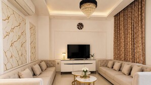 A modern living room with a sofa set, a TV, a chandelier, and a decorative plant.