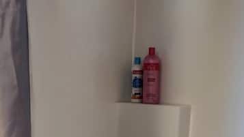 Ein Badezimmer mit Dusche, Toilette und Waschbecken. Zwei Flaschen hängen an der Wand.
