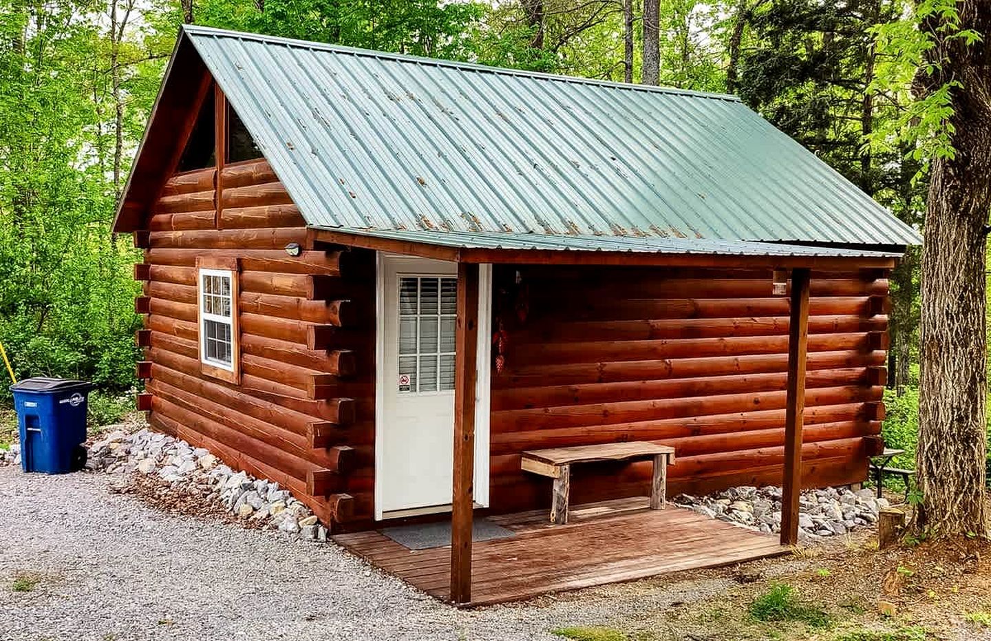 Una cabaña de troncos con un porche, una puerta y un banco pequeño.